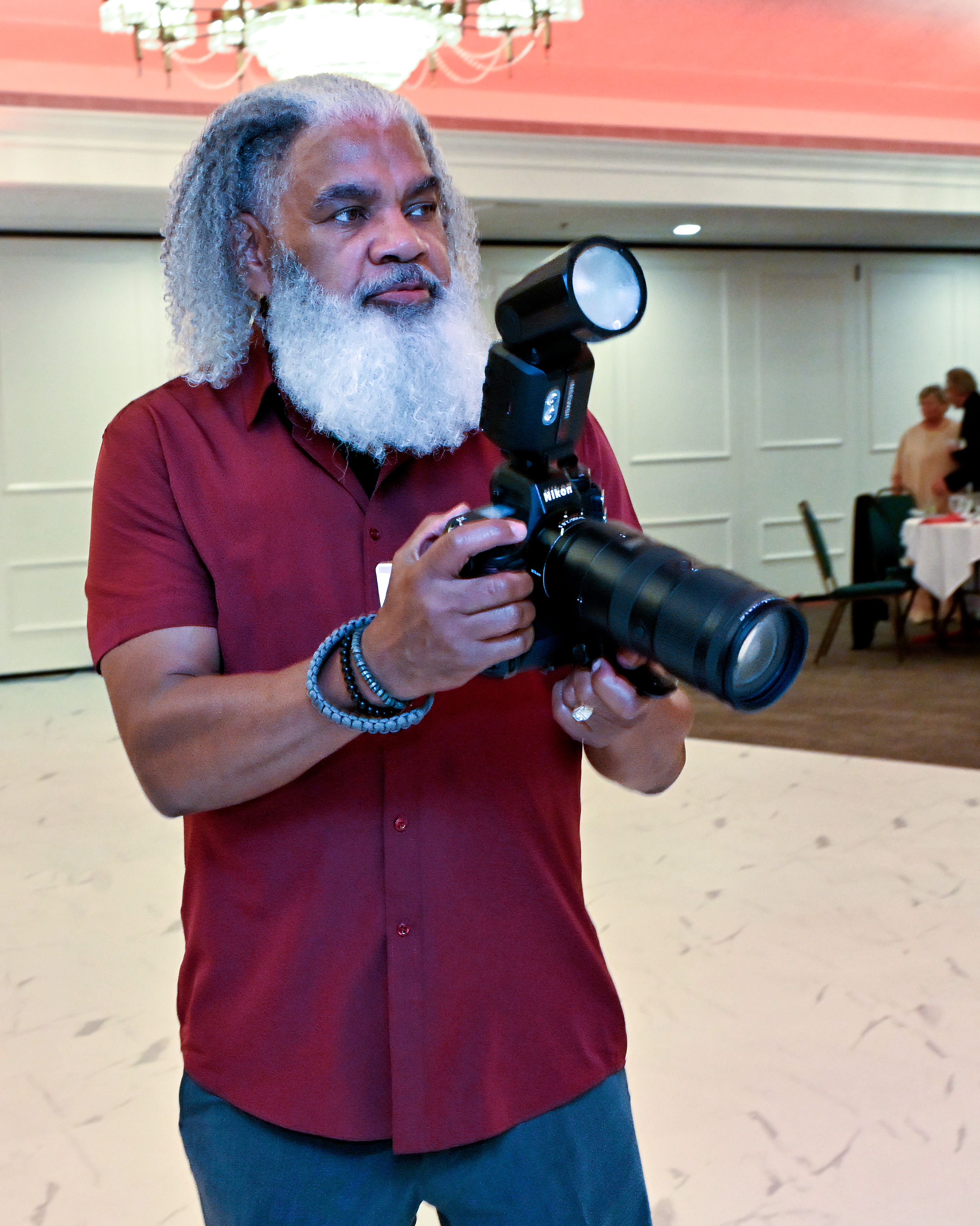 Leon McPherson holding a Nikon camera with an external flash at an indoor event